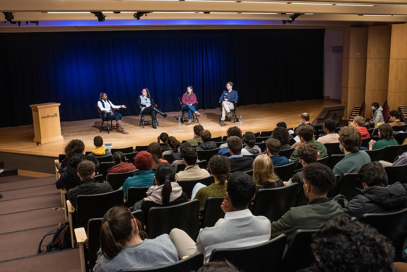 Four people on a stage before a large crowd