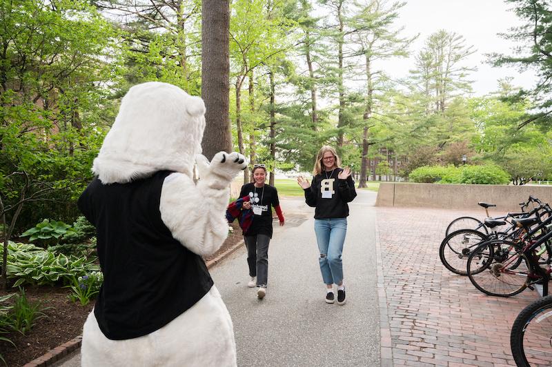 Two people walking towards Bowdoin polar bear mascot